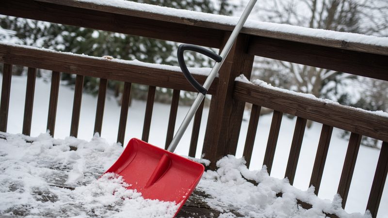 A red snow shovel with a second curved handle leaning on a snowy deck railing, in Minneapolis–St. Paul, Minnesota